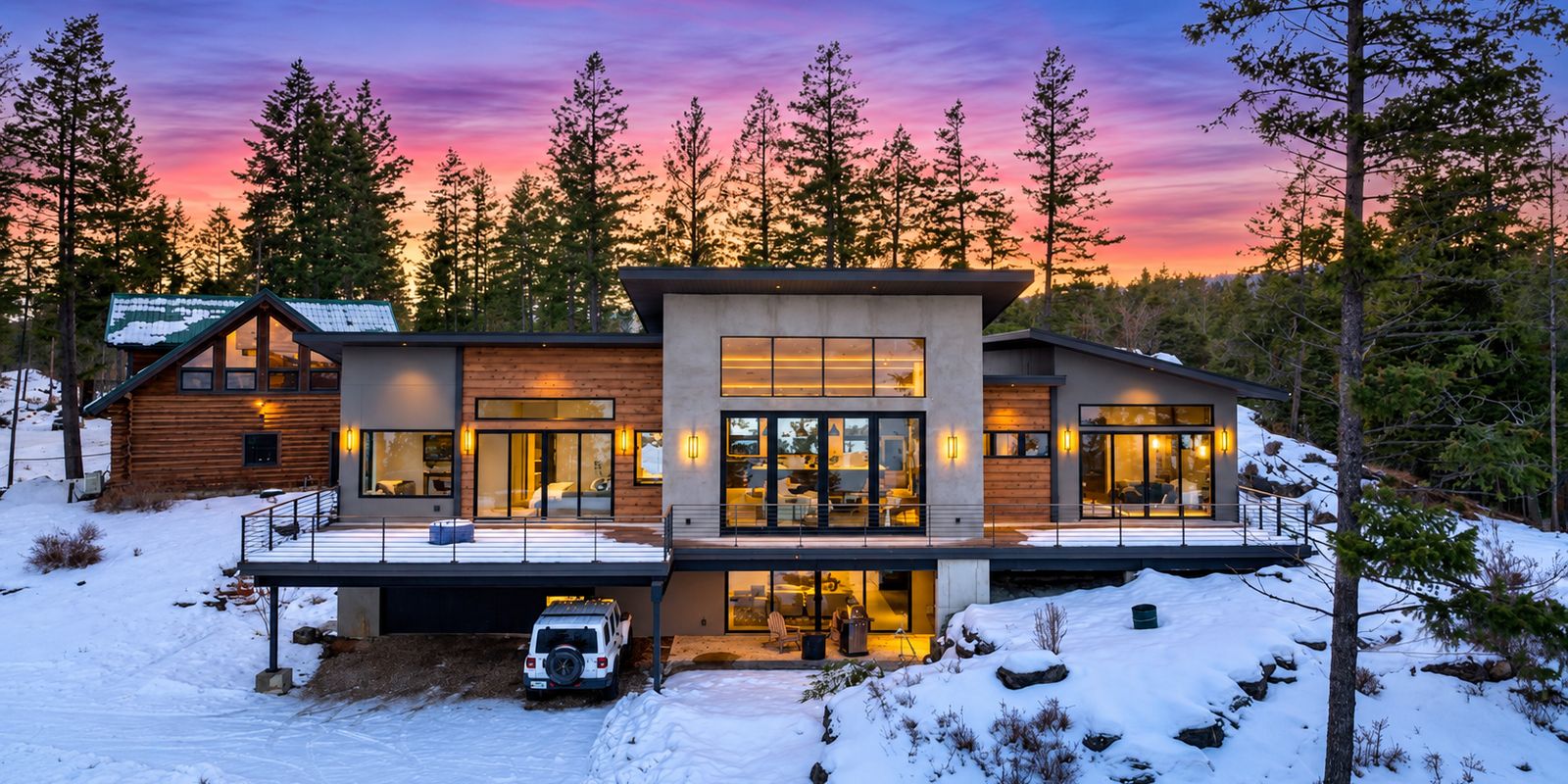 Modern mountain home with glowing windows among snowy pines at dusk