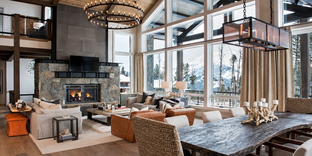 Great room with a stone fireplace, iron chandeliers and tall windows facing snowy mountains