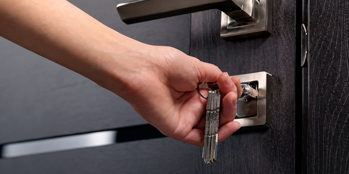 Hand turning a key in the lock of a dark front door