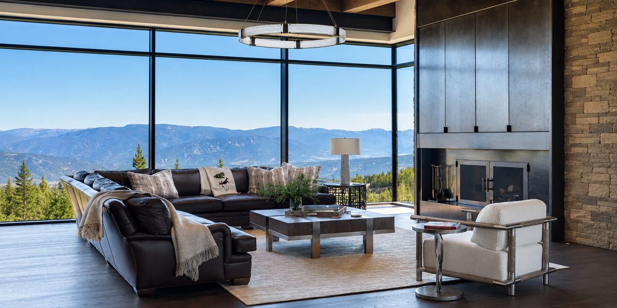Living room with a leather sectional and floor-to-ceiling windows overlooking forested mountains