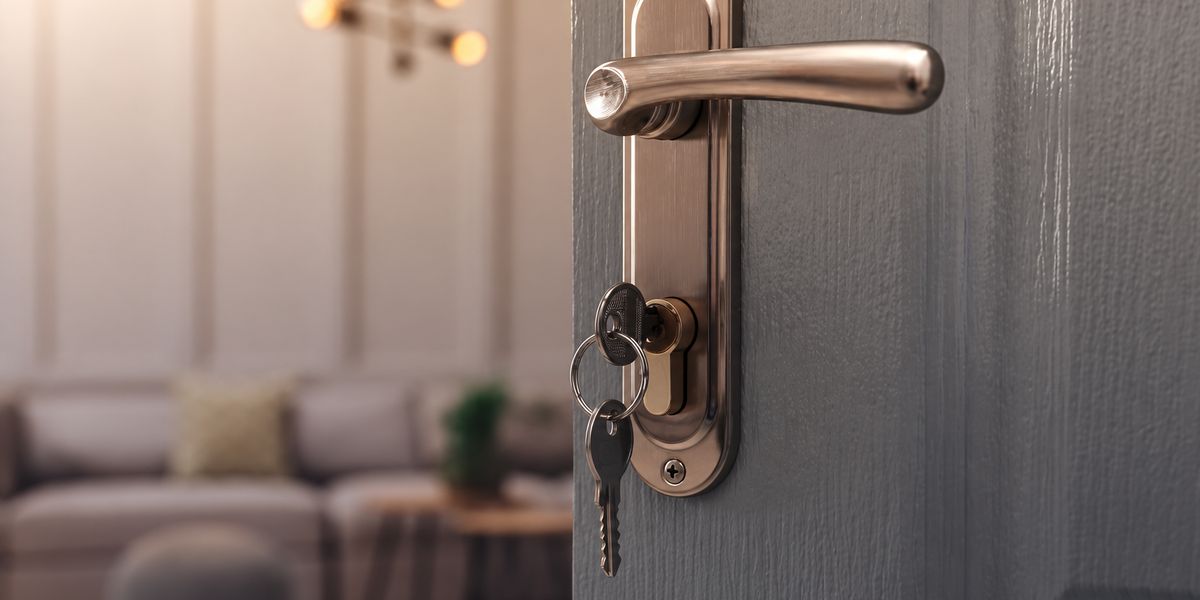 Front door ajar with keys in the lock and a softly lit living room beyond